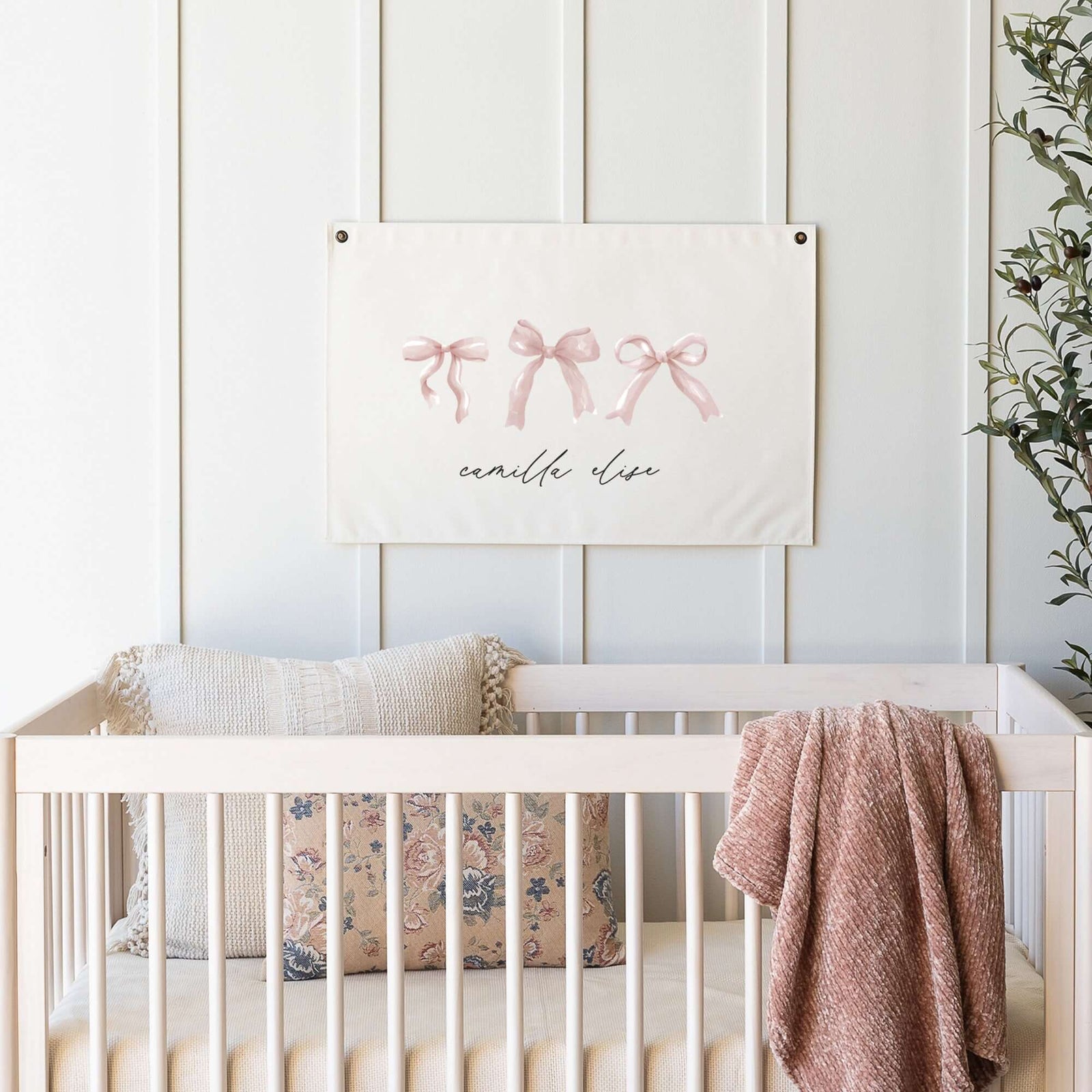 Custom baby name sign with pink bow designs and elegant calligraphy, showcased in a modern nursery setting with soft textiles, a floral pillow, and natural tones. A perfect choice for personalized nursery wall decor.