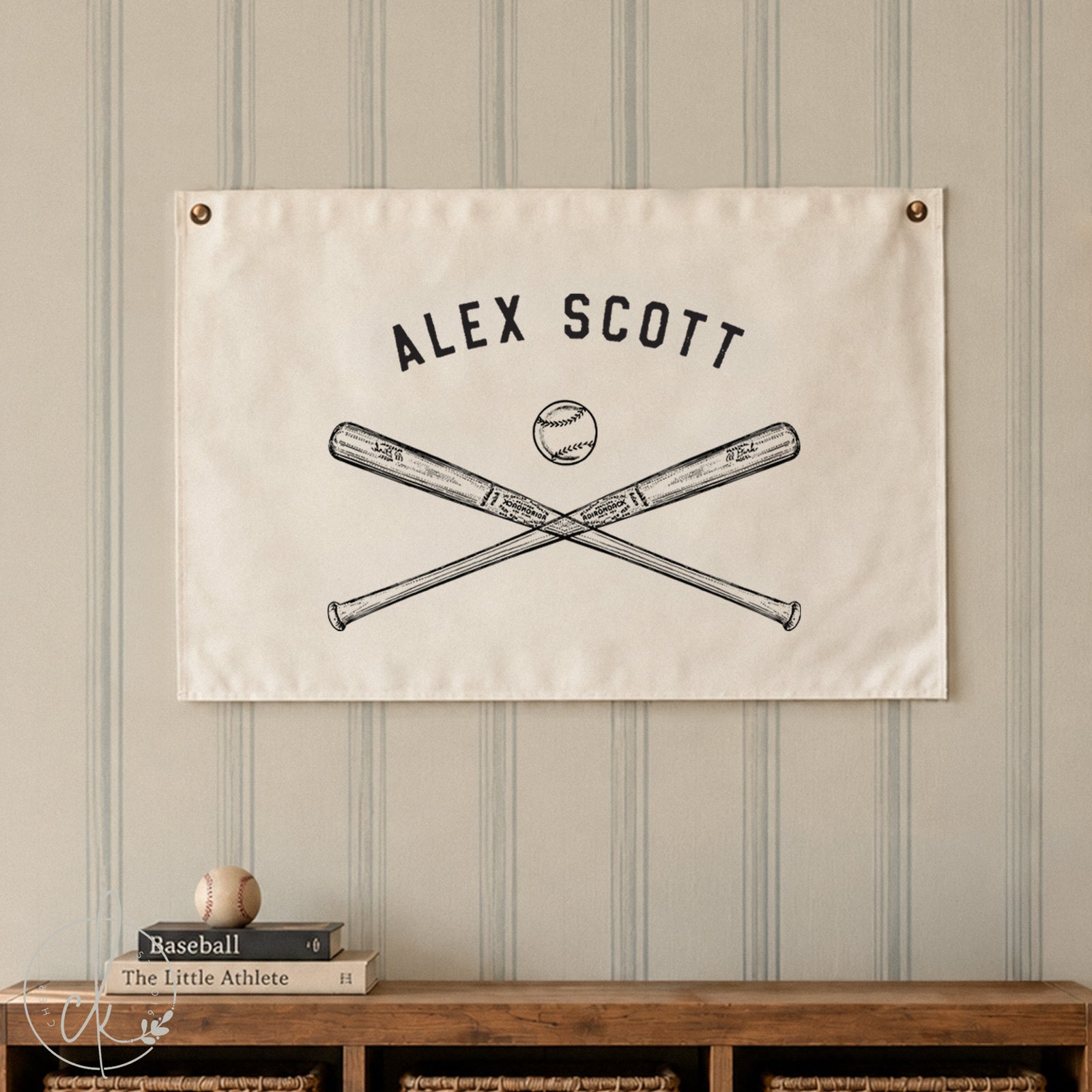 A personalized canvas flag with Alex Scott written above a sketch of crossed baseball bats and a baseball, hanging on a light blue paneled wall. Below the flag is a metal bench with a baseball glove and ball on top.