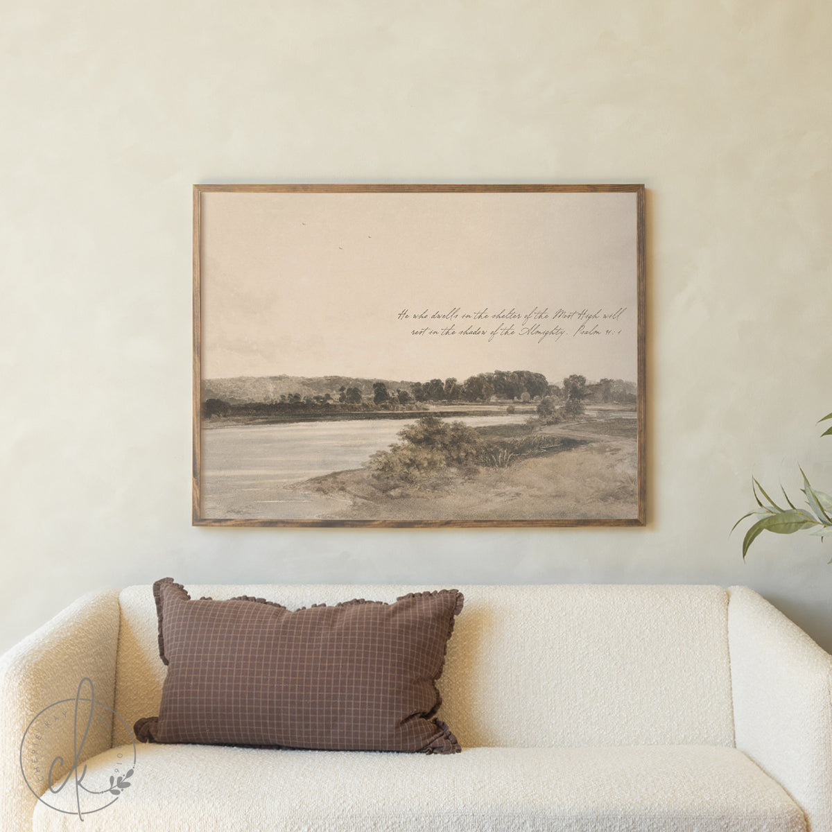 Framed landscape print on a wall above a sofa with a brown pillow.