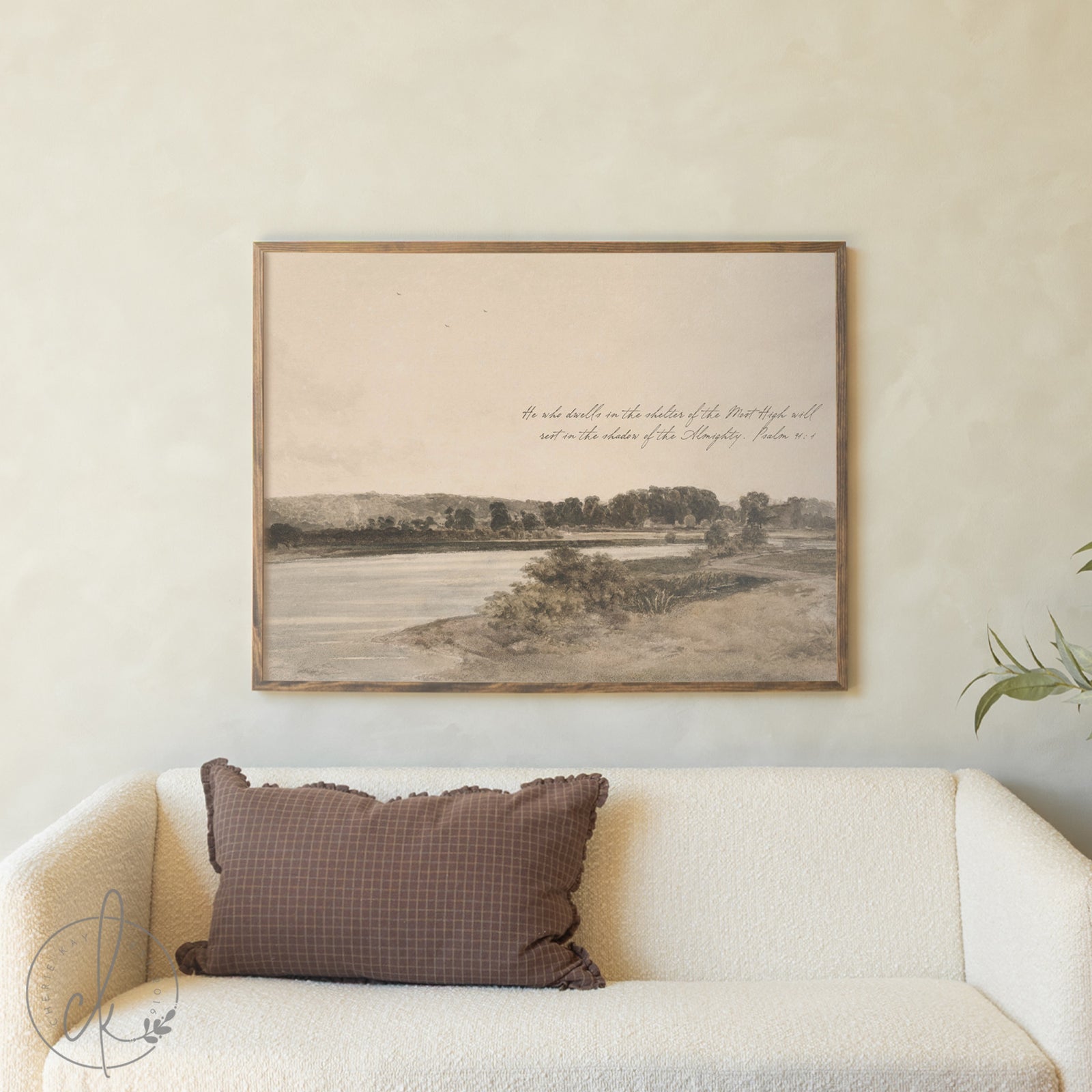 Framed landscape print on a wall above a sofa with a brown pillow.