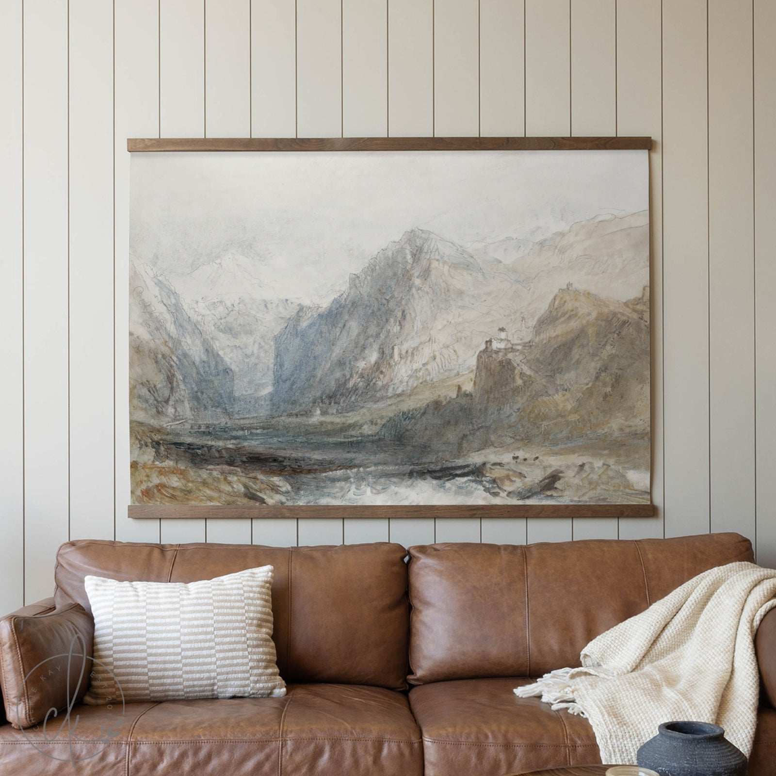 Brown leather sofa with a decorative pillow and blanket, featuring a large landscape painting of mountains on the wall.