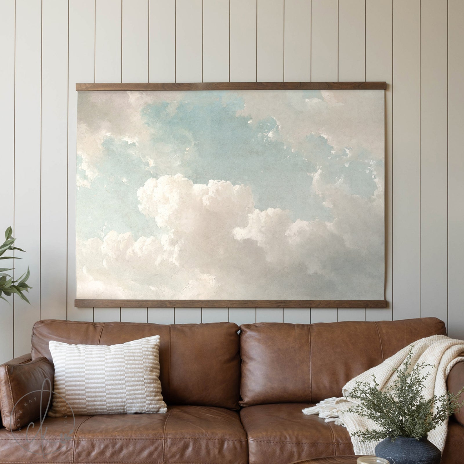 Brown leather sofa with a large framed artwork of clouds on a white paneled wall.