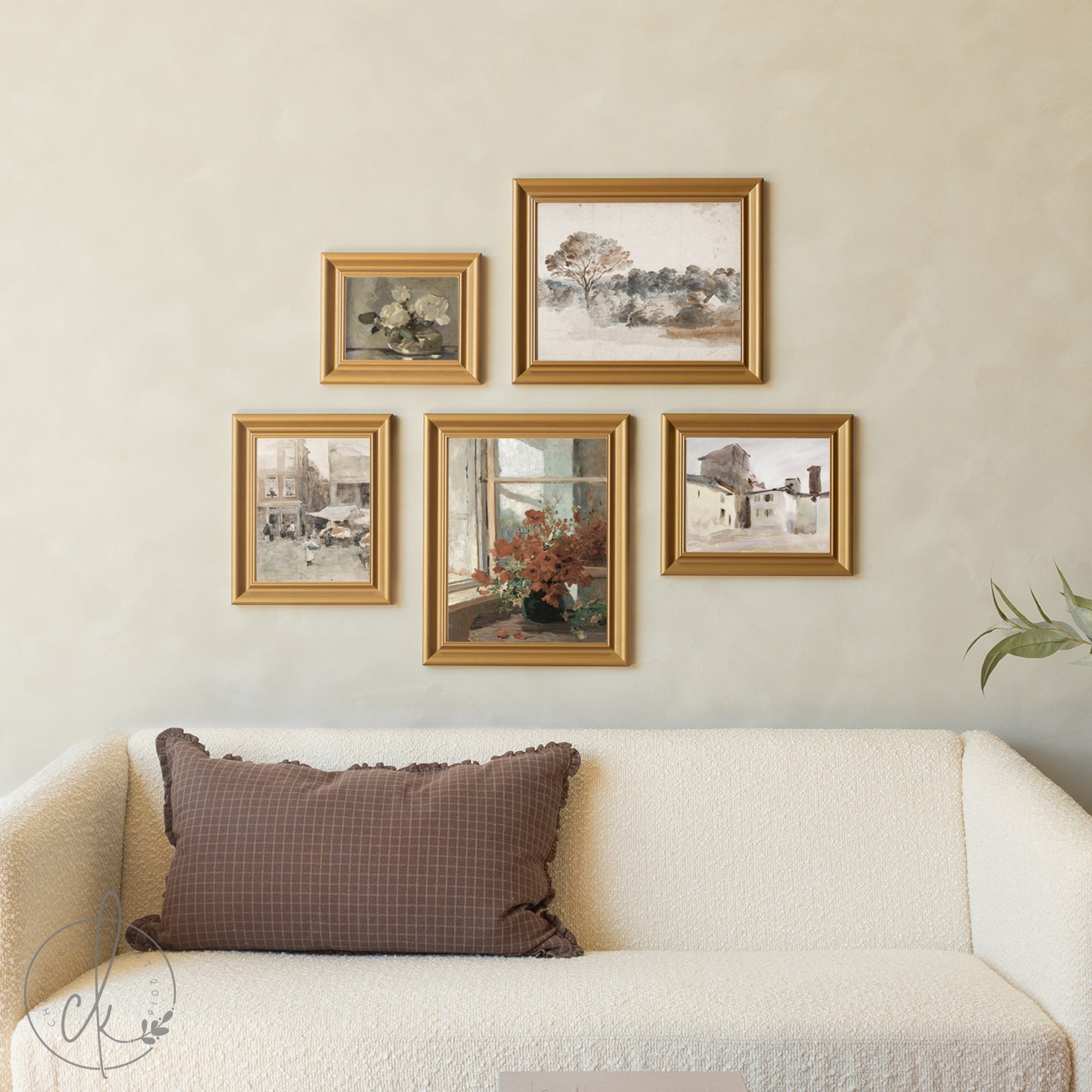 Framed artworks on a wall above a sofa with a decorative pillow.