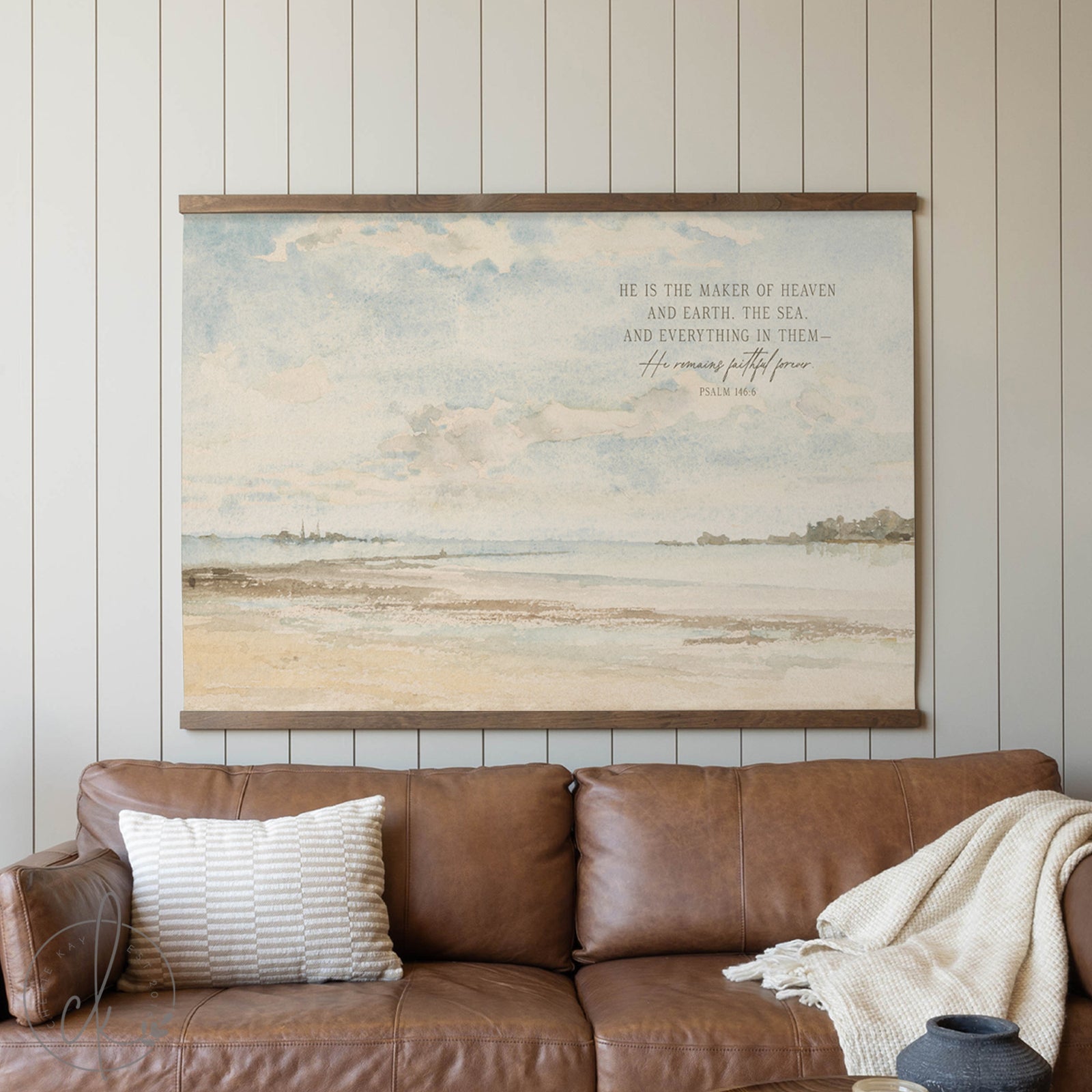 Framed landscape painting with text above a brown leather sofa in a room.