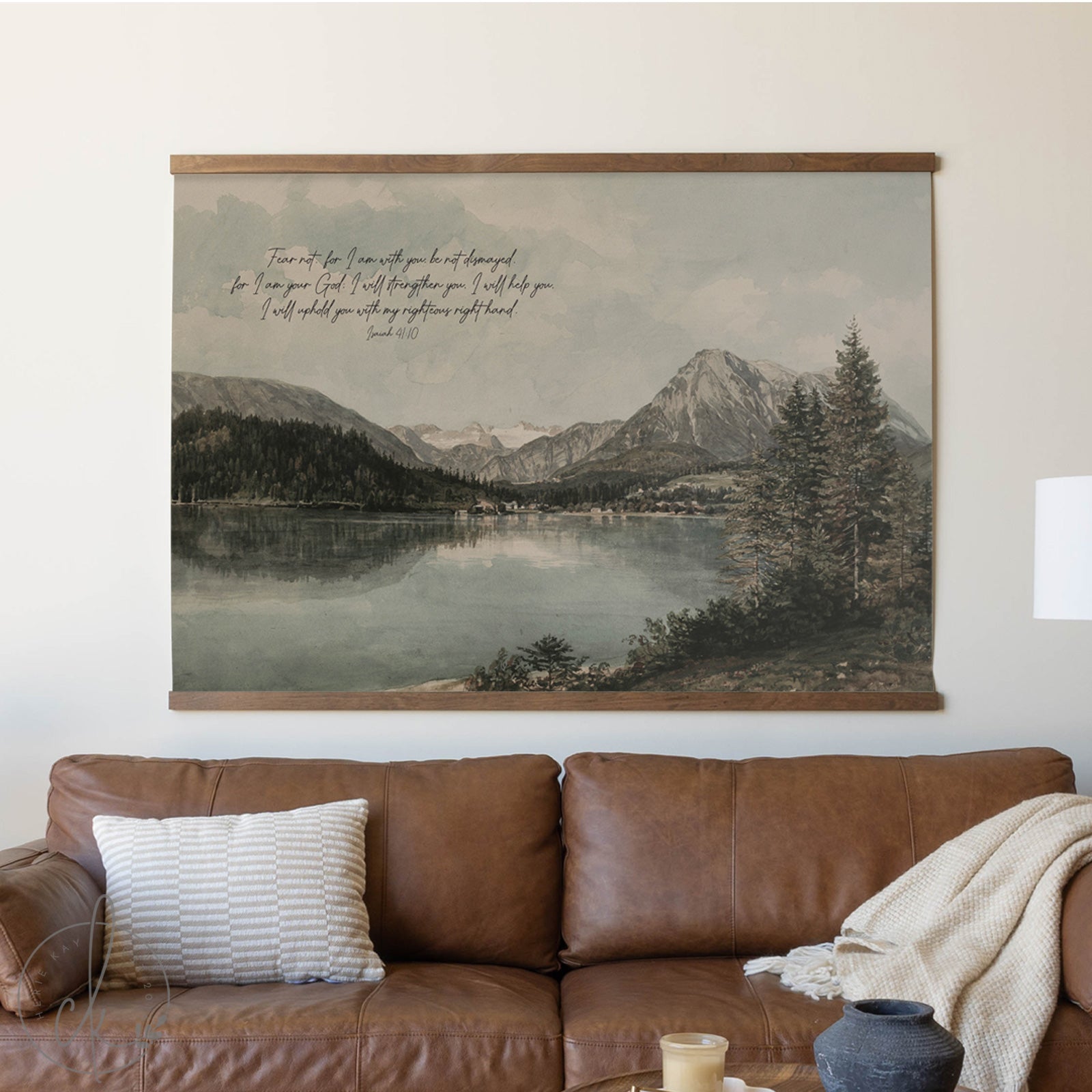 Framed landscape painting above a brown leather sofa with decorative pillows and a blanket.