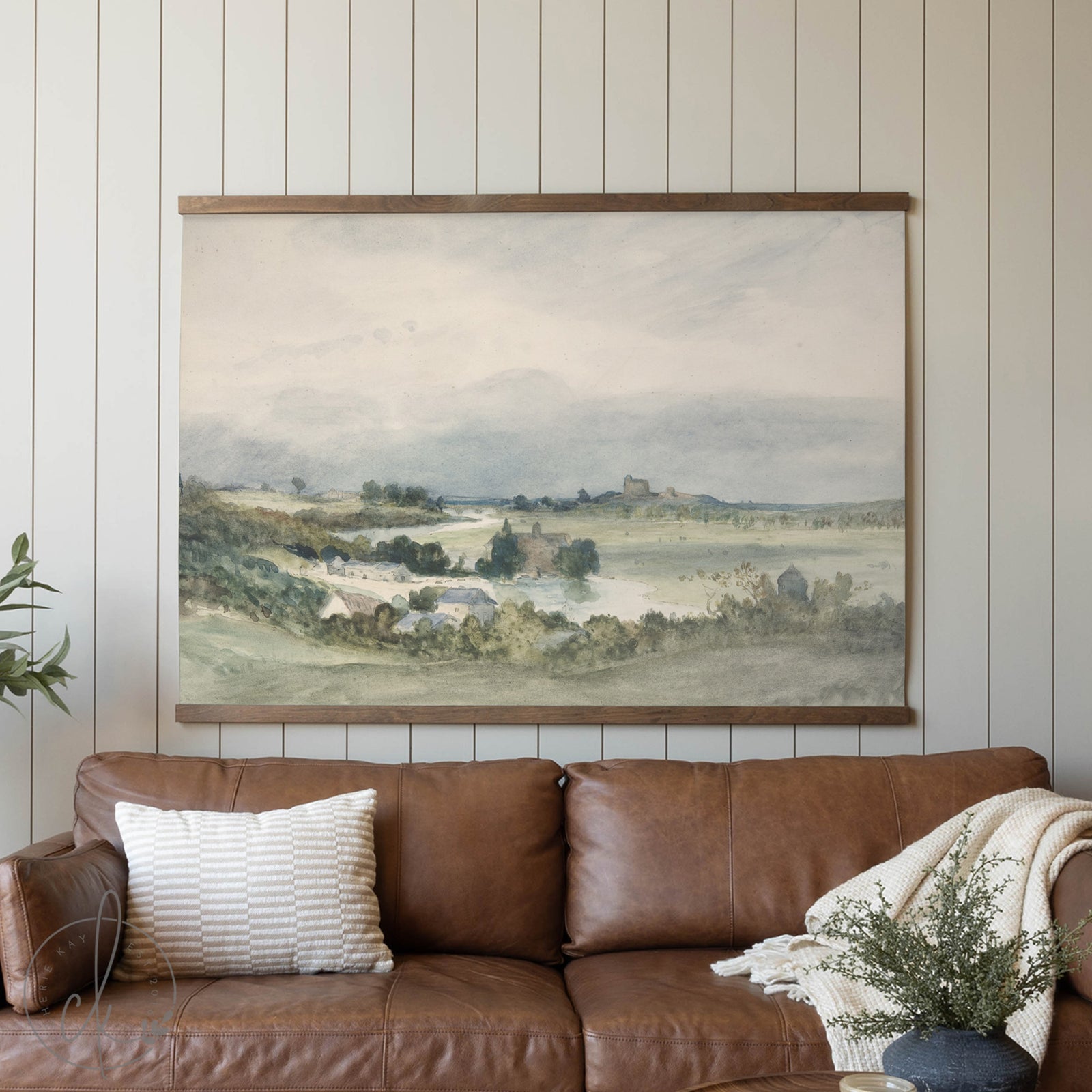 Framed landscape painting above a brown leather sofa in a living room.