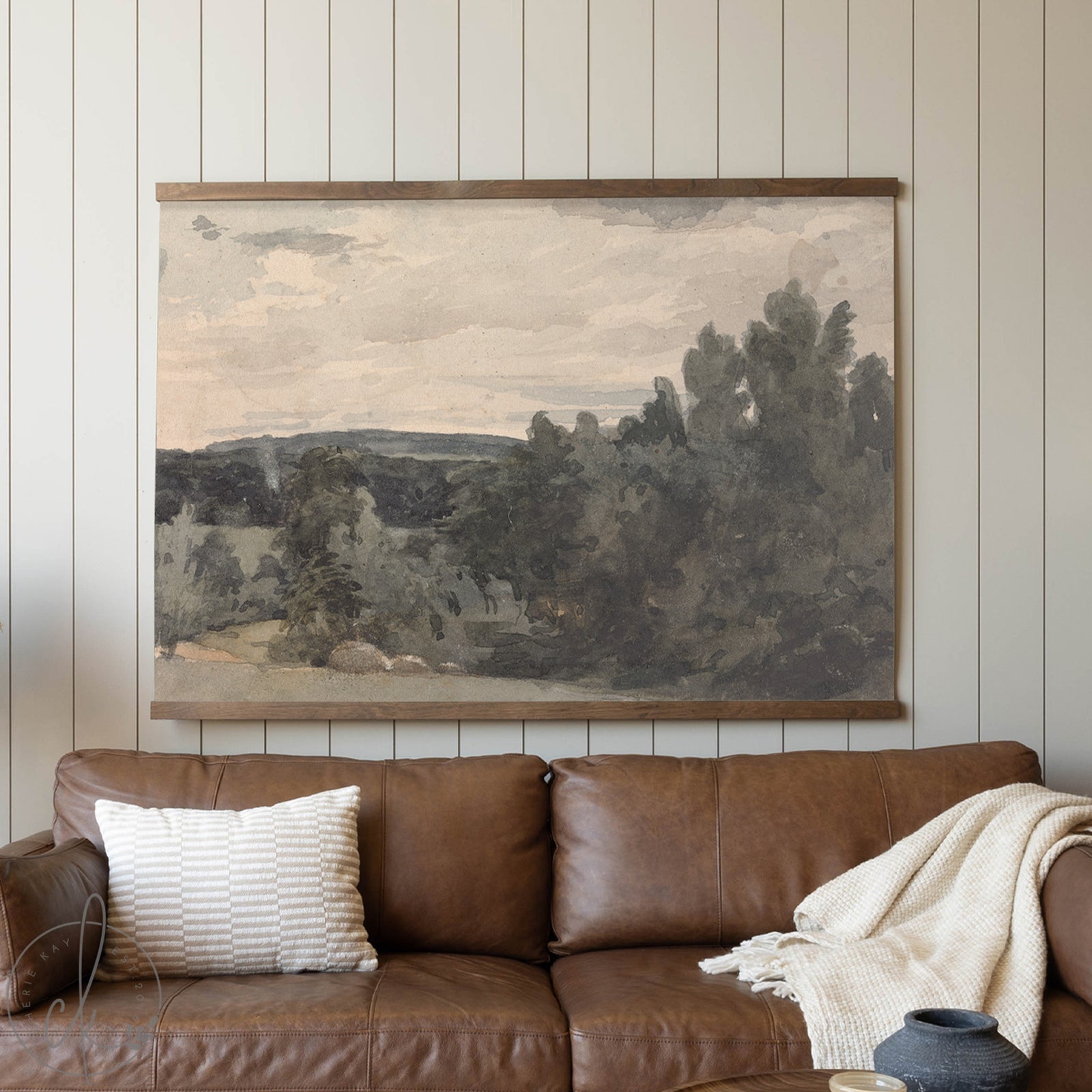 Landscape painting above a brown leather sofa with decorative pillows and a blanket.