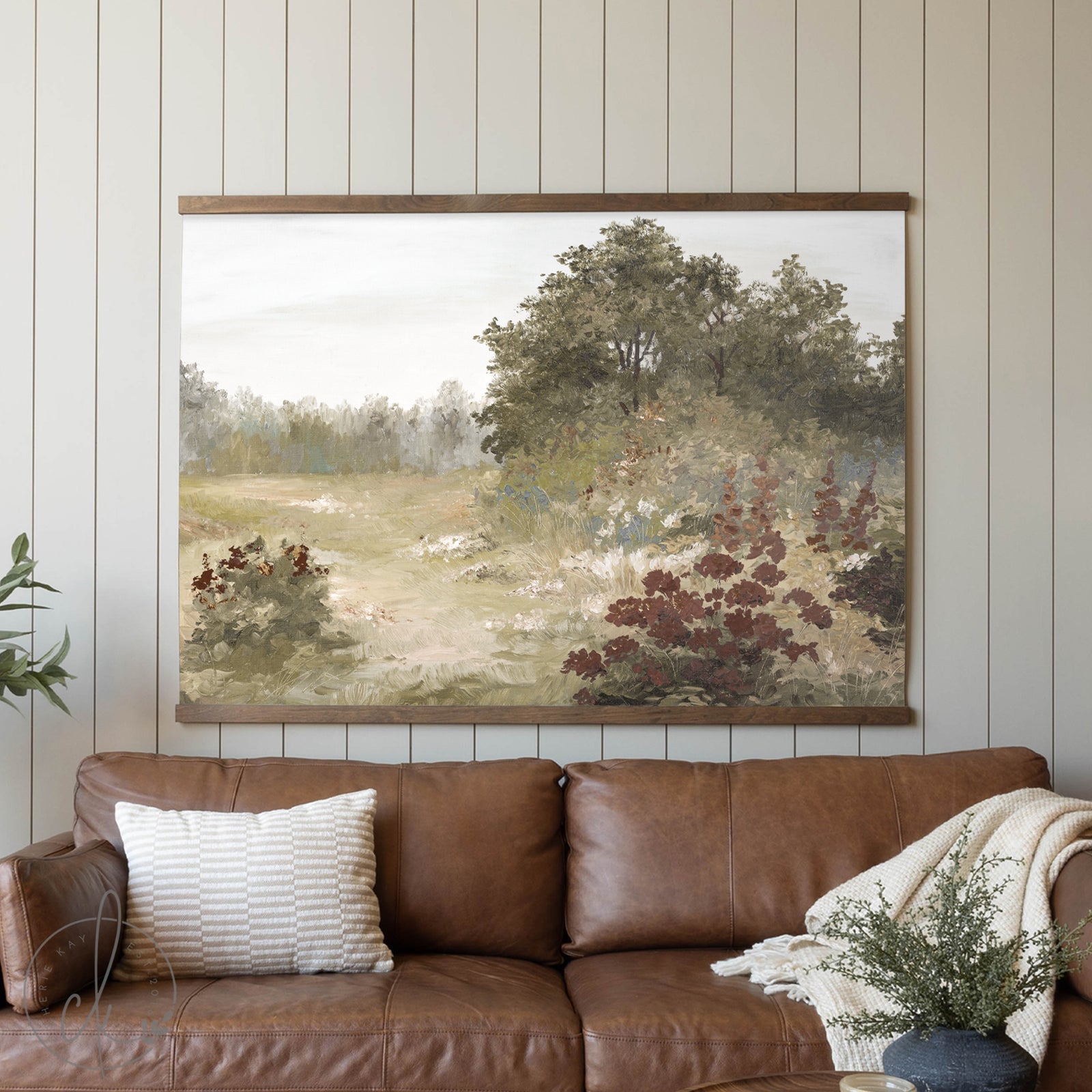 Framed landscape painting above a brown leather sofa in a living room.