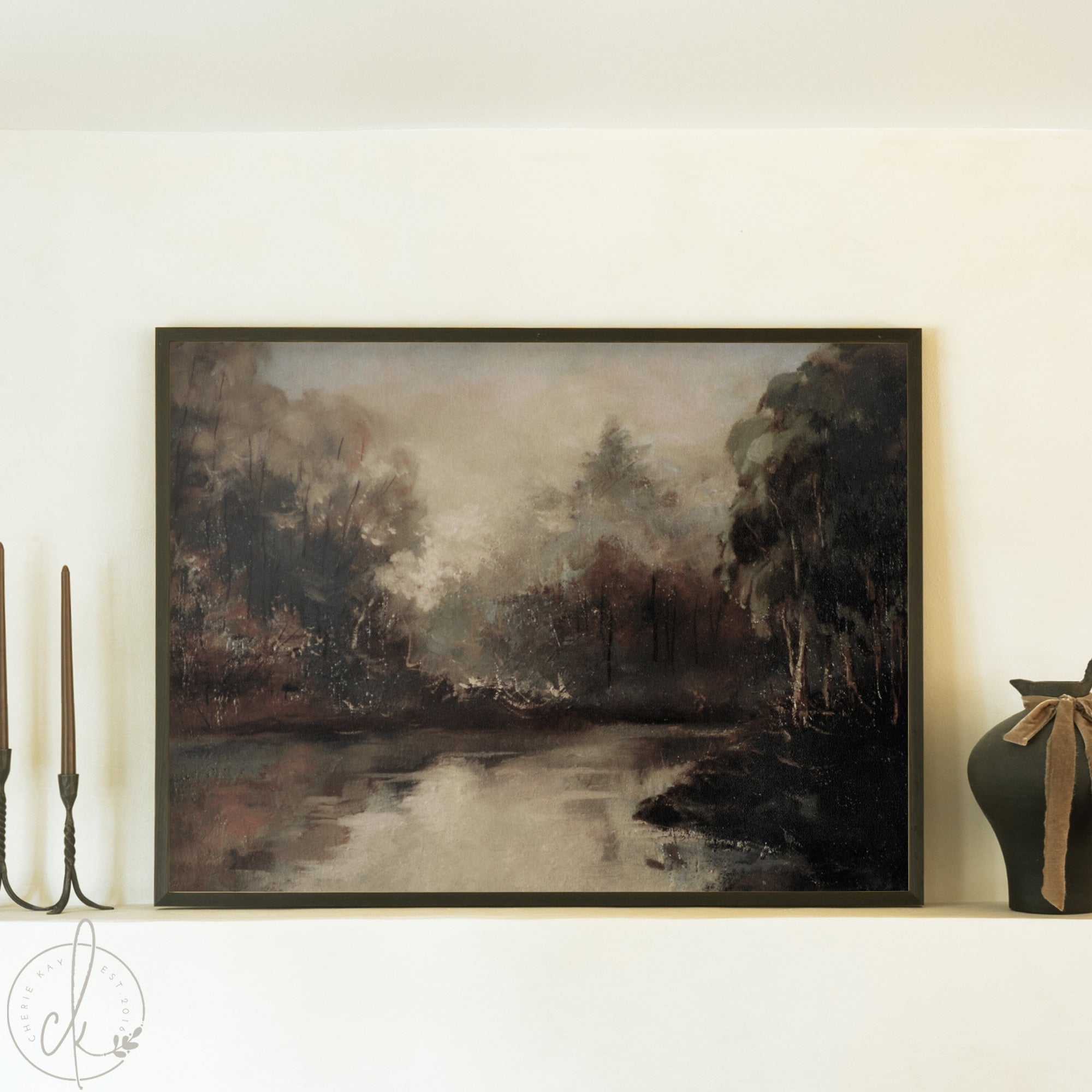 Framed landscape painting of a forest scene with a river on a white wall.