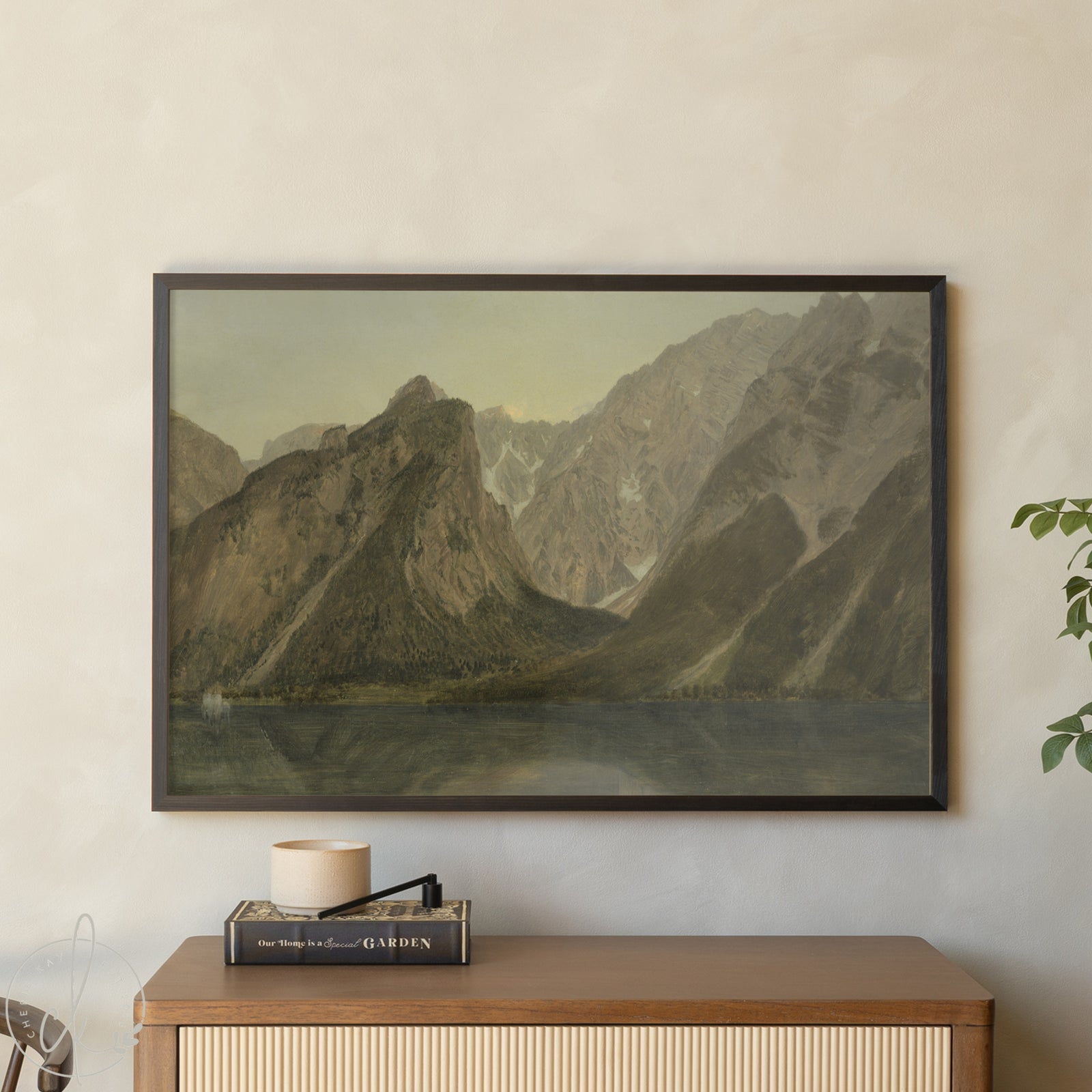 Framed mountain landscape print on a wall above a wooden cabinet.