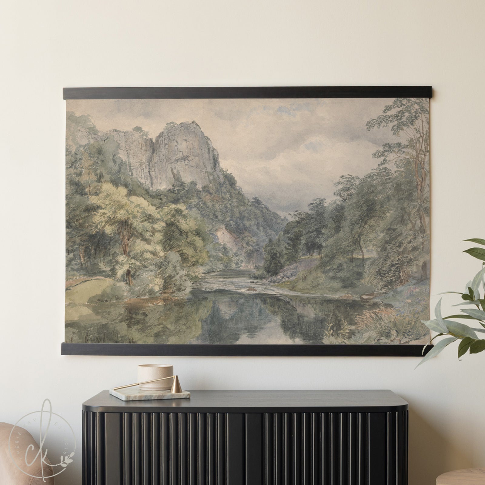 Roll-up landscape with a river and mountains displayed on a wall above a black cabinet.