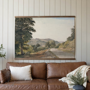 Brown leather sofa with a landscape painting on the wall in a living room setting.