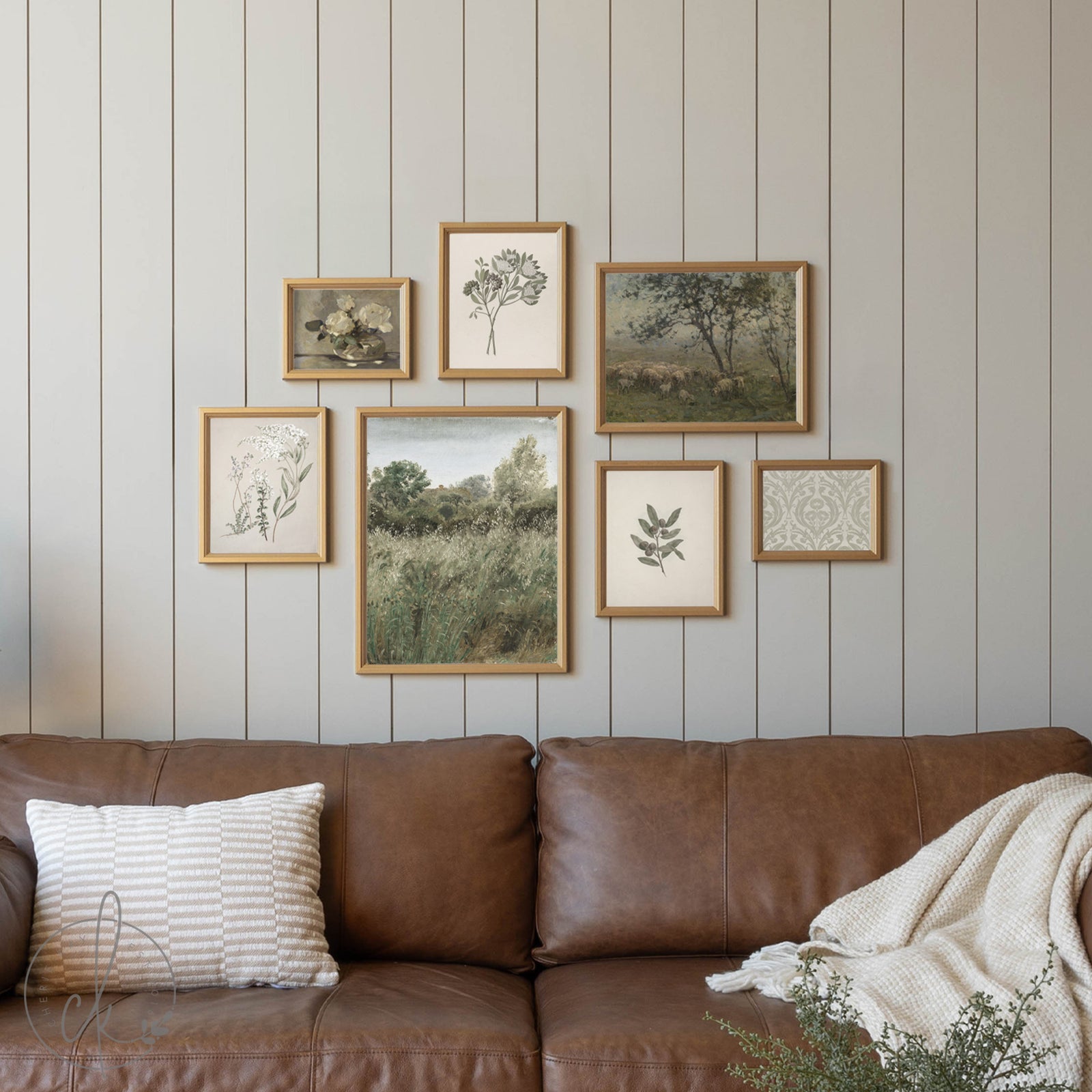Brown leather sofa with decorative pillows and a blanket against a wall with framed botanical prints.