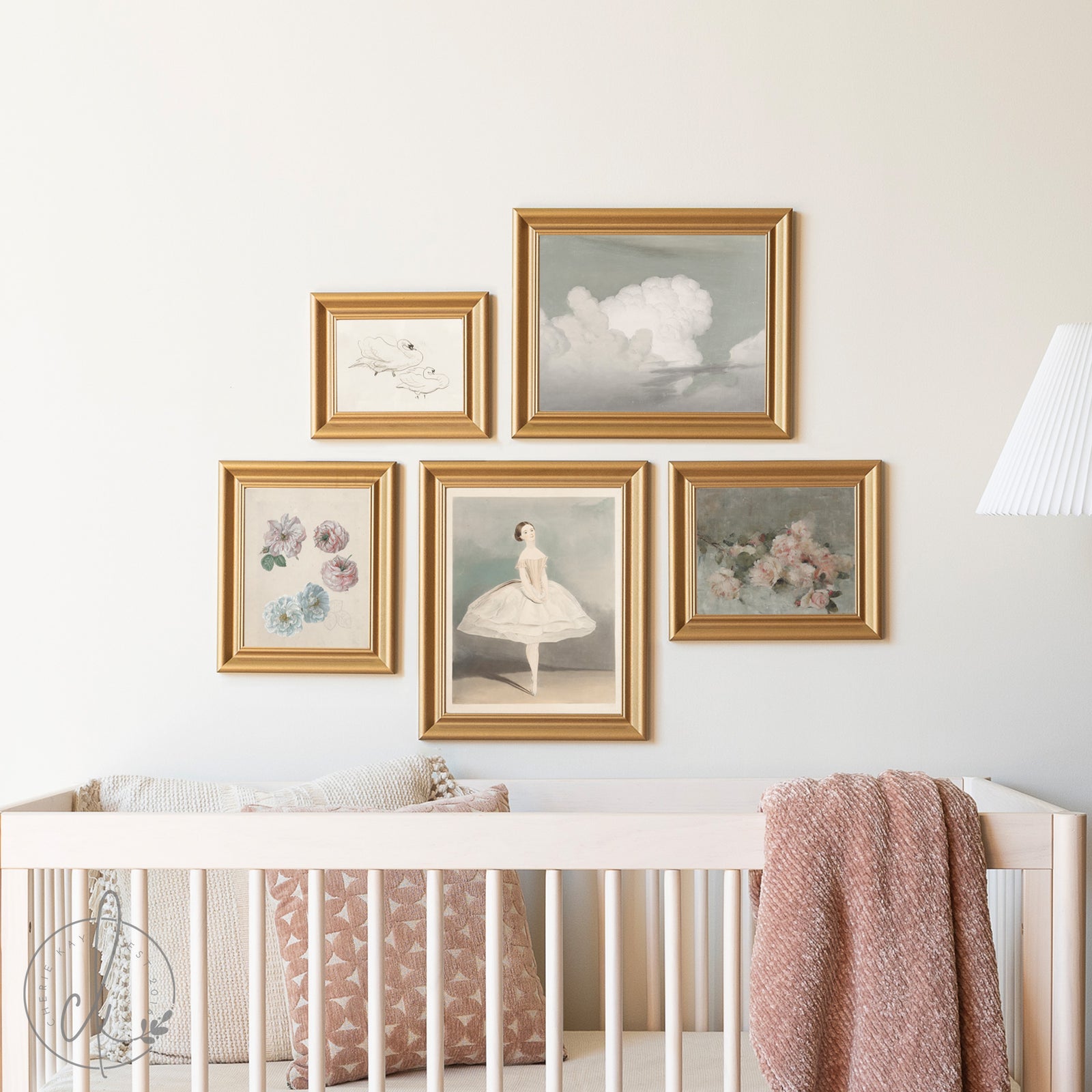 Framed artworks on a wall above a crib with a pink blanket