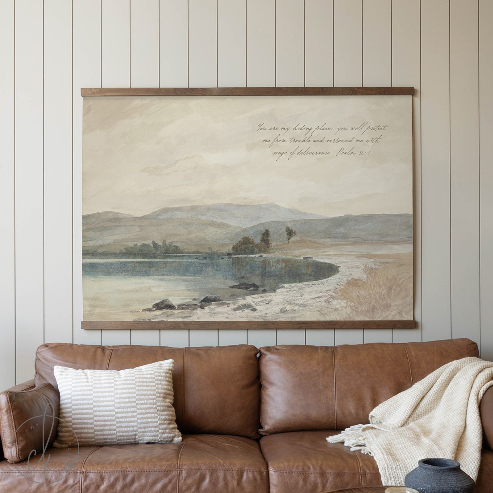 Framed landscape painting above a brown leather sofa with decorative pillows and a blanket.