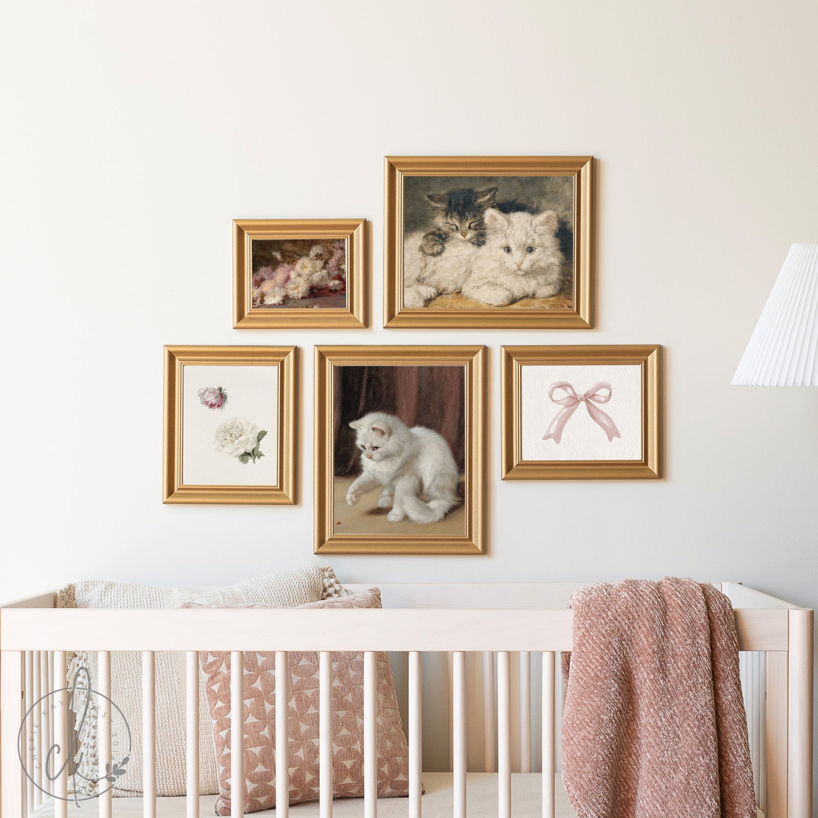 Framed pictures of cats on a wall above a crib with pink blanket
