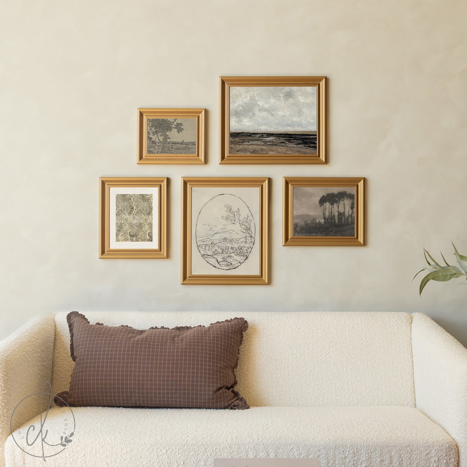 Framed artworks on a wall above a sofa with a brown pillow.