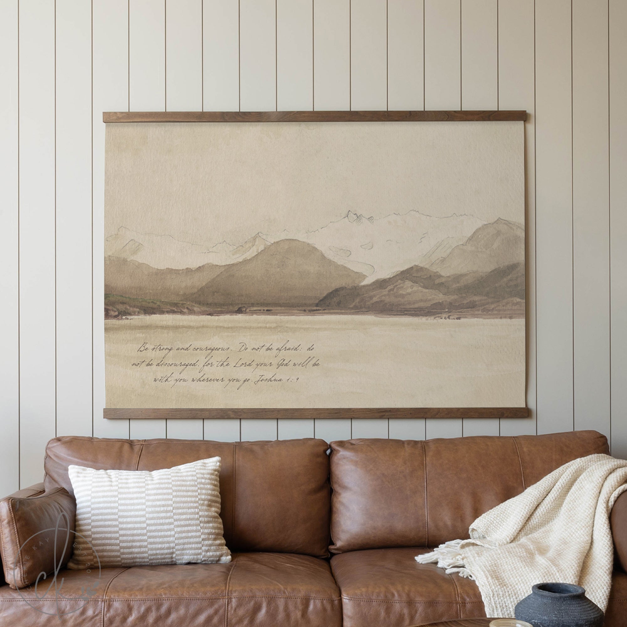 Brown leather sofa with a decorative pillow and blanket, featuring a large framed landscape painting on the wall.