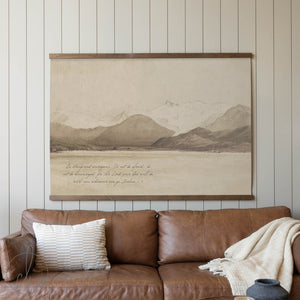 Brown leather sofa with a decorative pillow and blanket, featuring a large framed landscape painting on the wall.