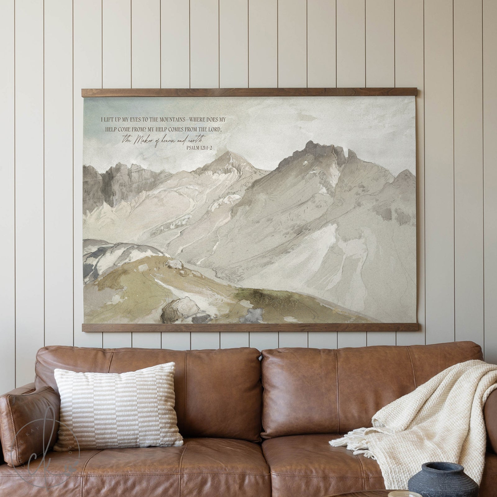 Brown leather sofa with a mountain landscape painting above it on a wooden wall.