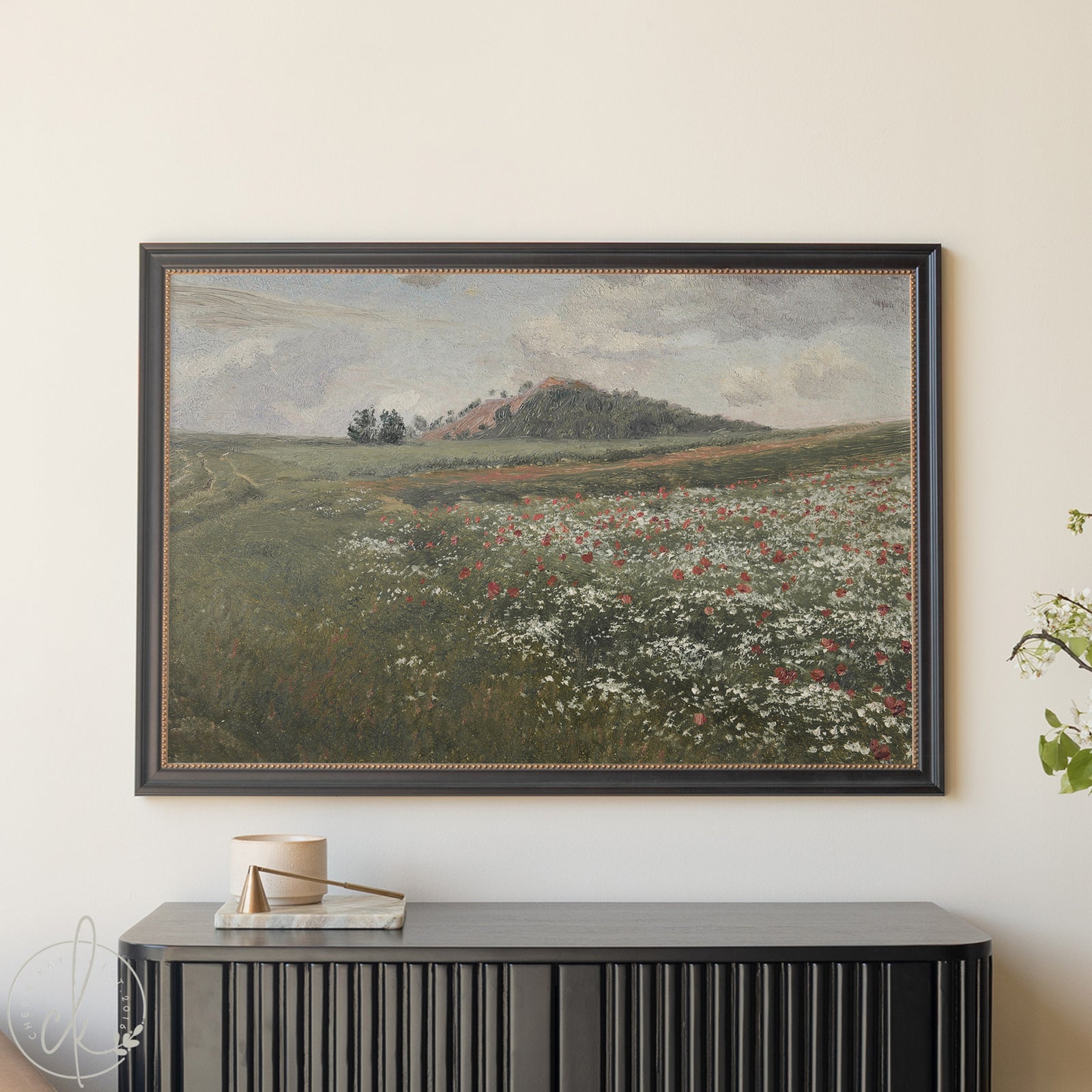 Framed landscape painting of a field with flowers on a wall above a black console table.