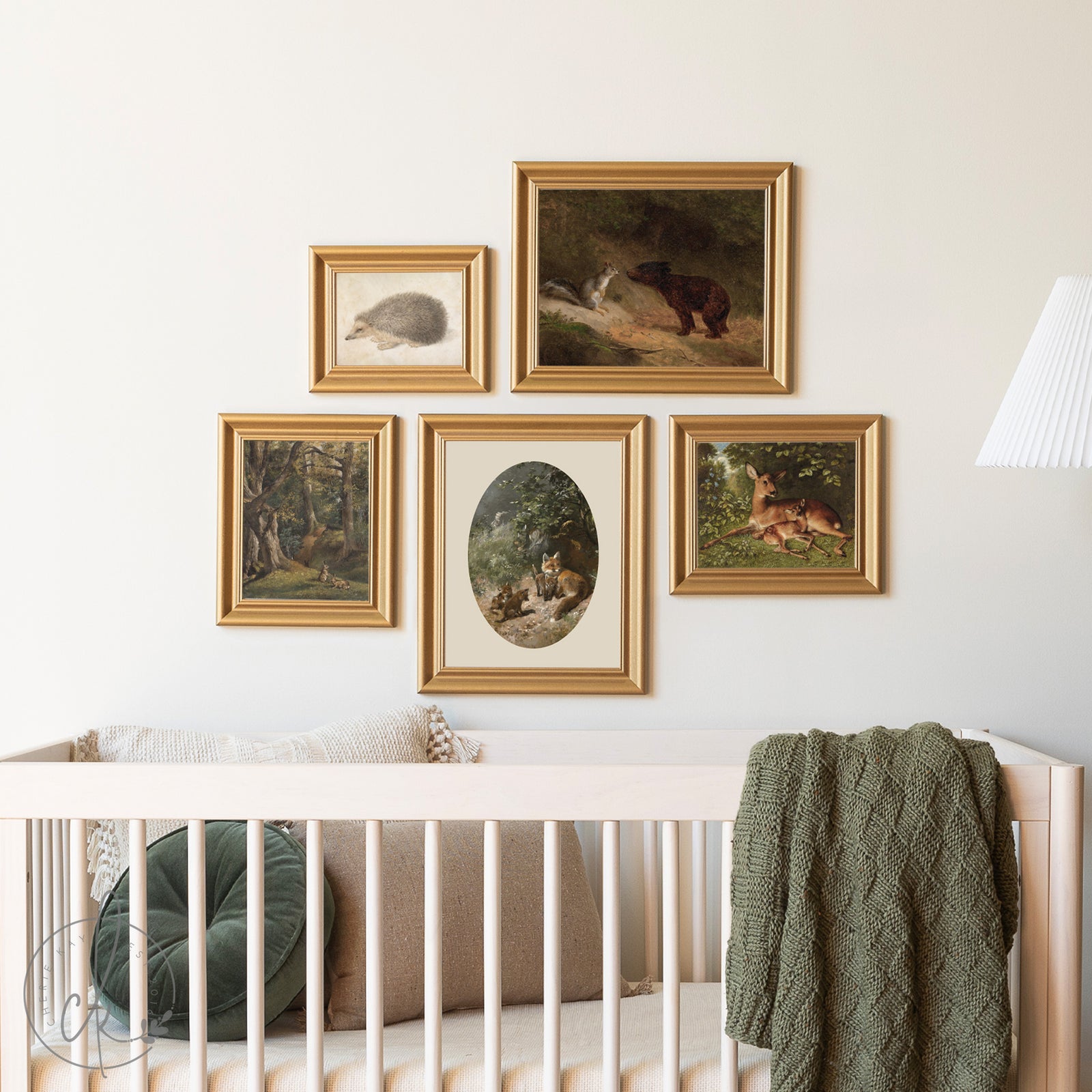 Framed animal paintings on a wall above a crib with green blanket and pillow.