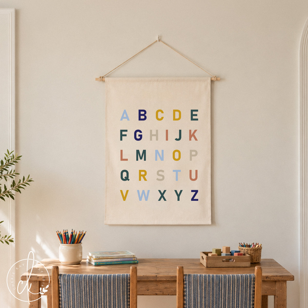 Fabric wall hanging ABC alphabet sign on cream canvas with multicolor letters, hung by a white string on a dowel rod.