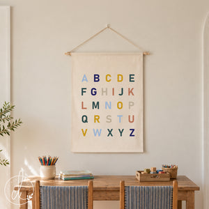 Fabric wall hanging ABC alphabet sign on cream canvas with multicolor letters, hung by a white string on a dowel rod.