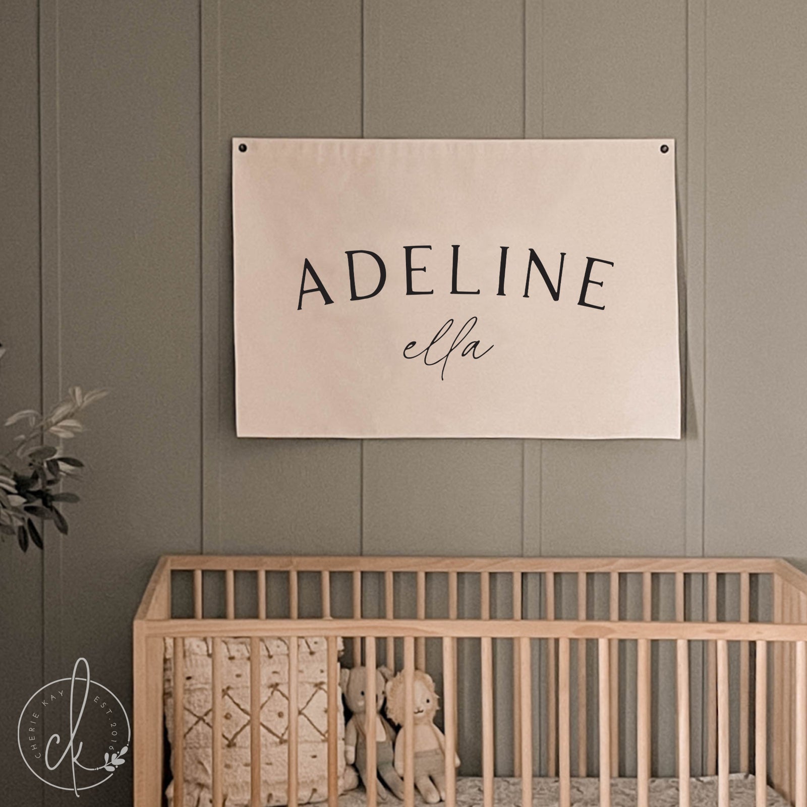 Personalized baby girl name canvas sign hanging above a wooden crib in a neutral-toned nursery, in elegant black fonts. Ideal for nursery decor, baby shower gifts, or newborn keepsakes.