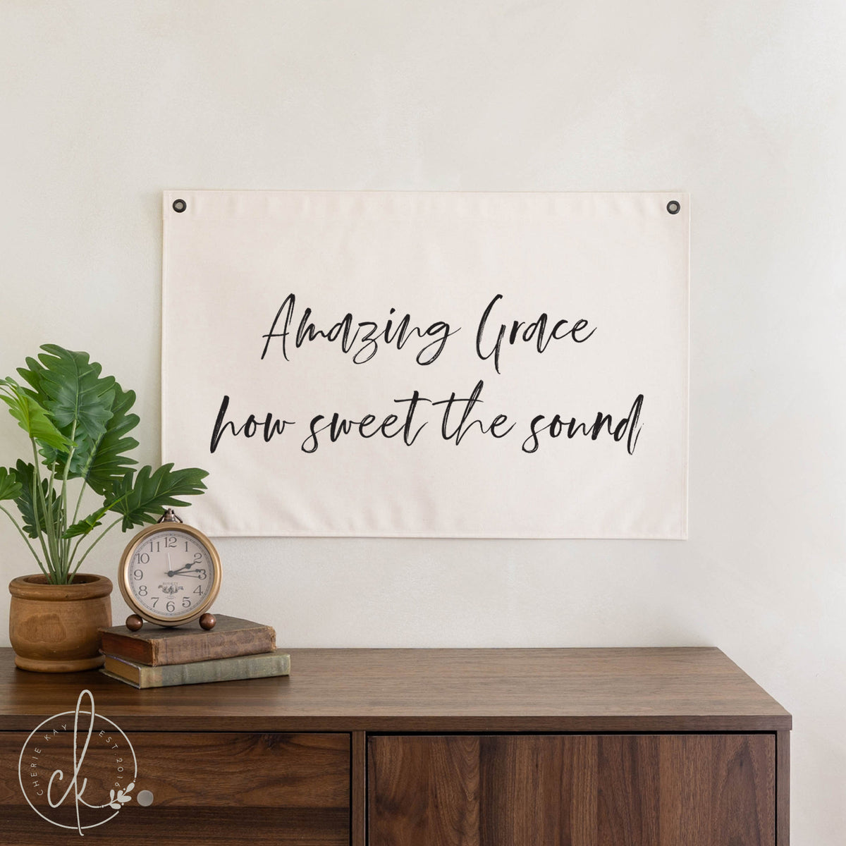 Decorative banner with &#39;Amazing Grace, how sweet the sound&#39; text above a wooden desk with a plant and clock.