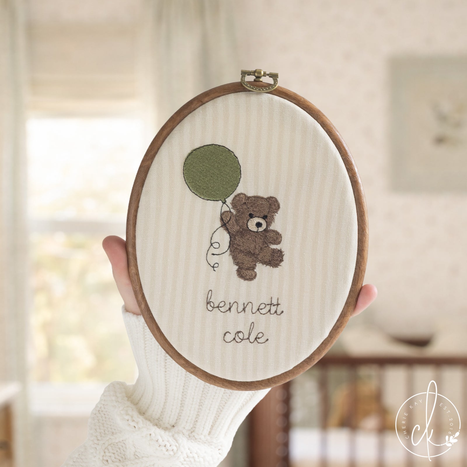 Embroidered teddy bear nursery decor with personalized baby name in oval hoop with brass hardware