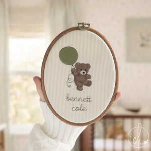 Embroidered teddy bear nursery decor with personalized baby name in oval hoop with brass hardware