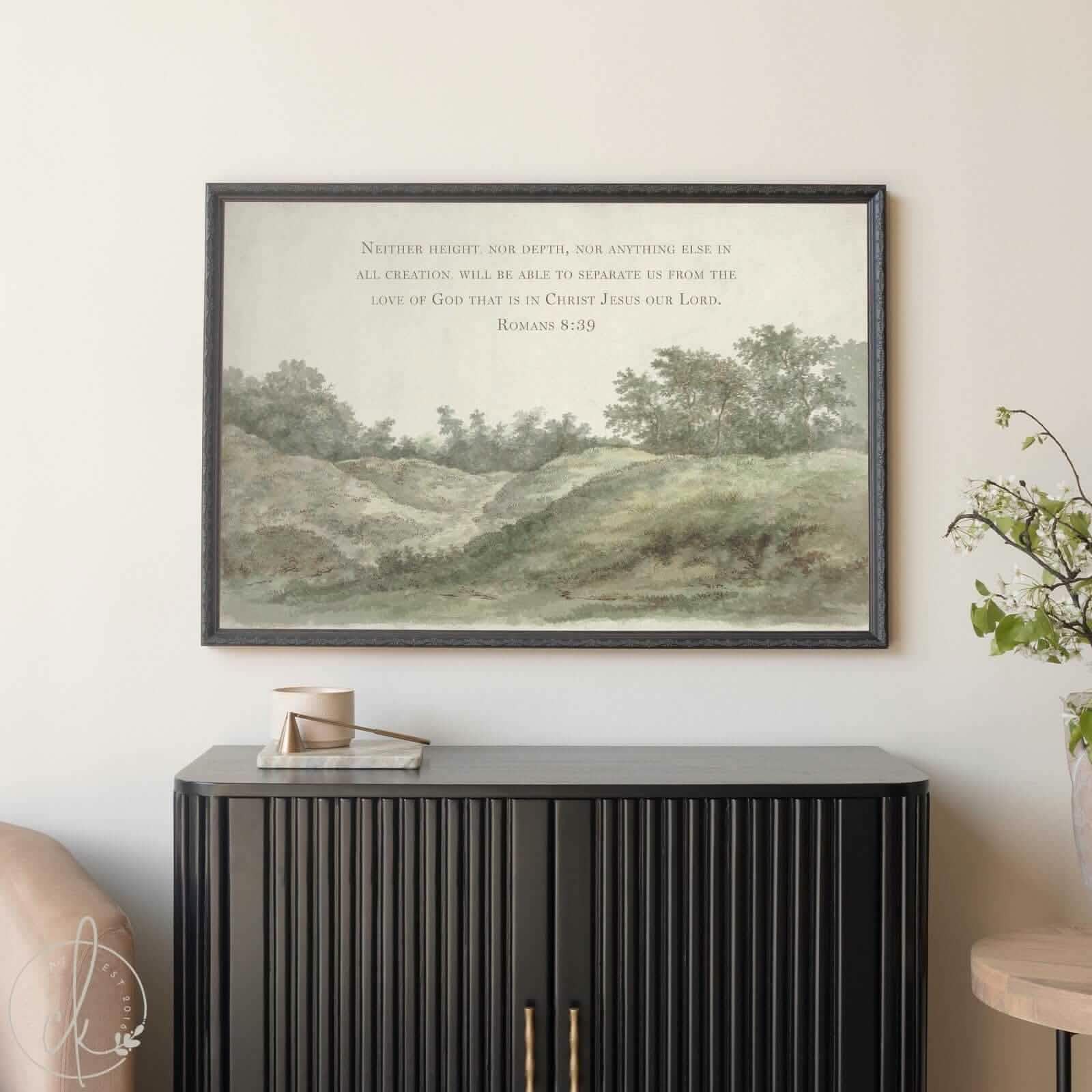 Framed vintage landscape art with Romans 8:39 Bible verse, featuring a peaceful green hillside and trees, styled above a modern black cabinet in a neutral-toned living space. Christian wall decor for entryway or living room.