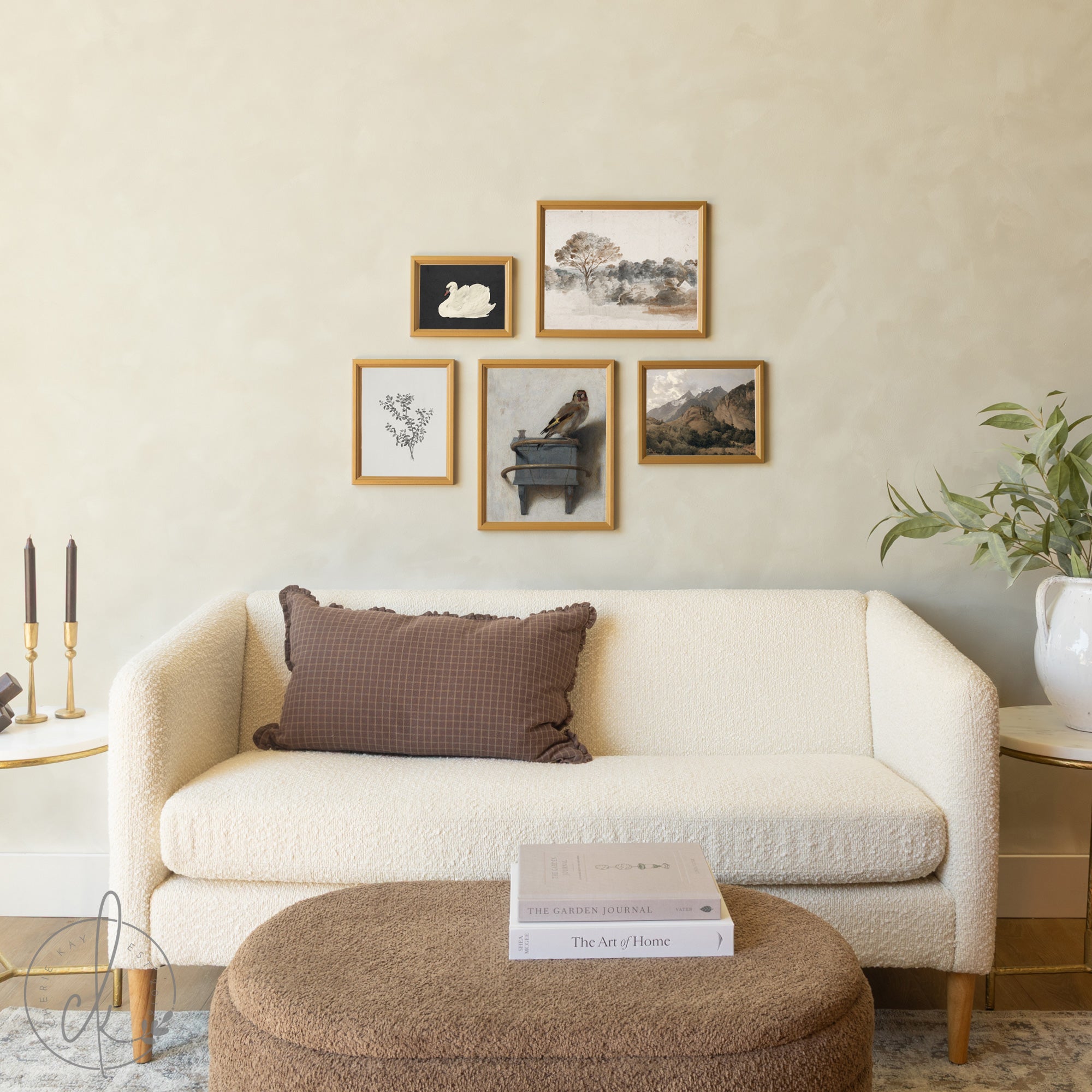 Five gold-framed artworks displayed in a gallery wall arrangement above a white sofa, featuring a mix of nature-themed pieces including a white swan silhouette, landscape watercolor, botanical print, bird on books still life, and mountain scene.