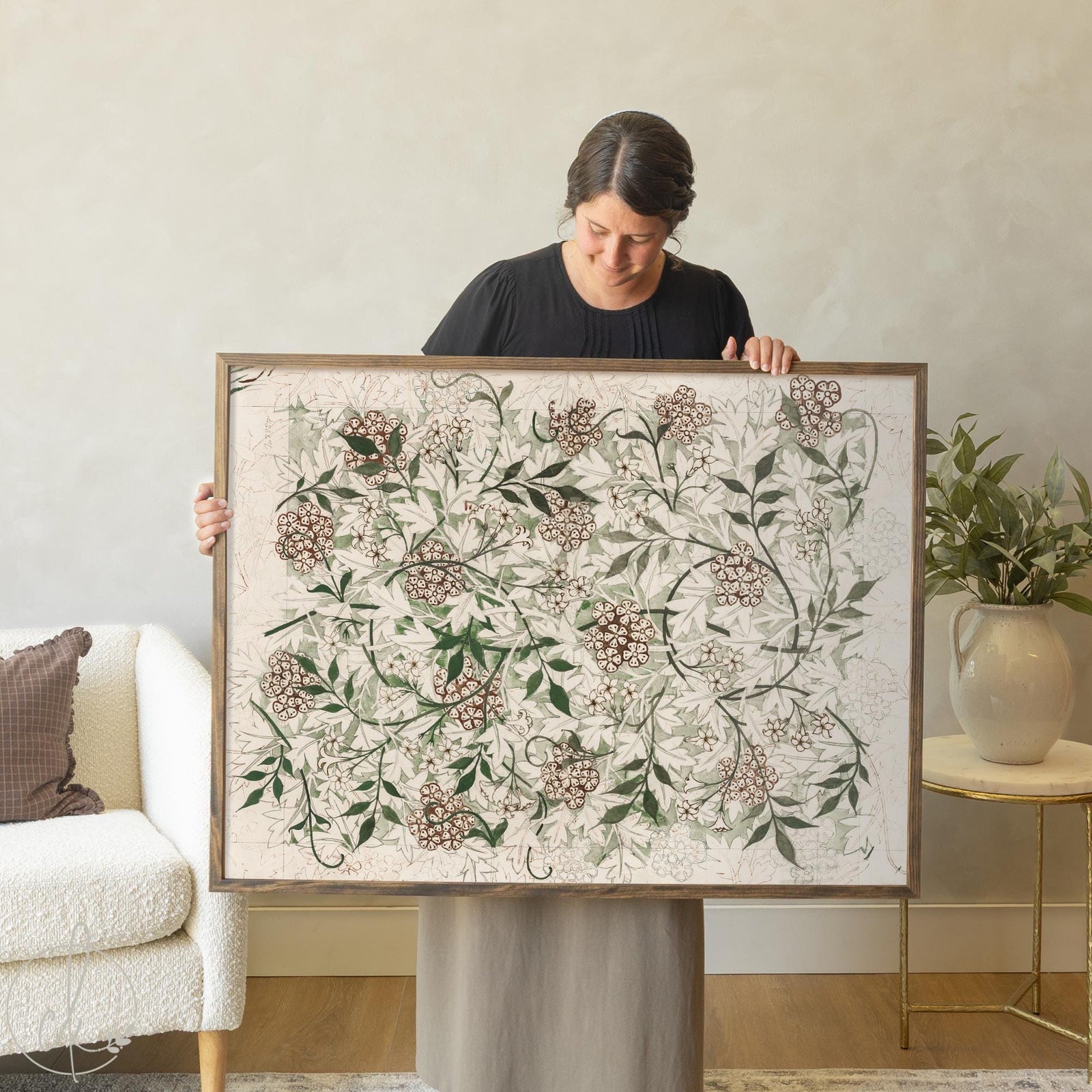 Woman holding large framed William Morris botanical wall art featuring pink wildflower clusters and green foliage pattern on cream background, vintage floral print in gold frame for living room decor