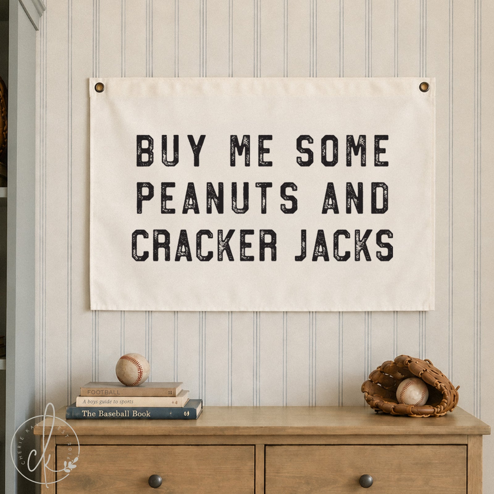 Baseball-themed canvas wall art with Buy Me Some Peanuts and Cracker Jacks text hanging in a sports-themed kids' room with metal bench, basketball, and baseball glove decor.