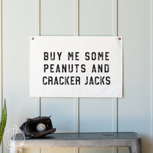 Sign with text 'Buy me some peanuts and cracker jacks' on a wall above a baseball glove and ball.
