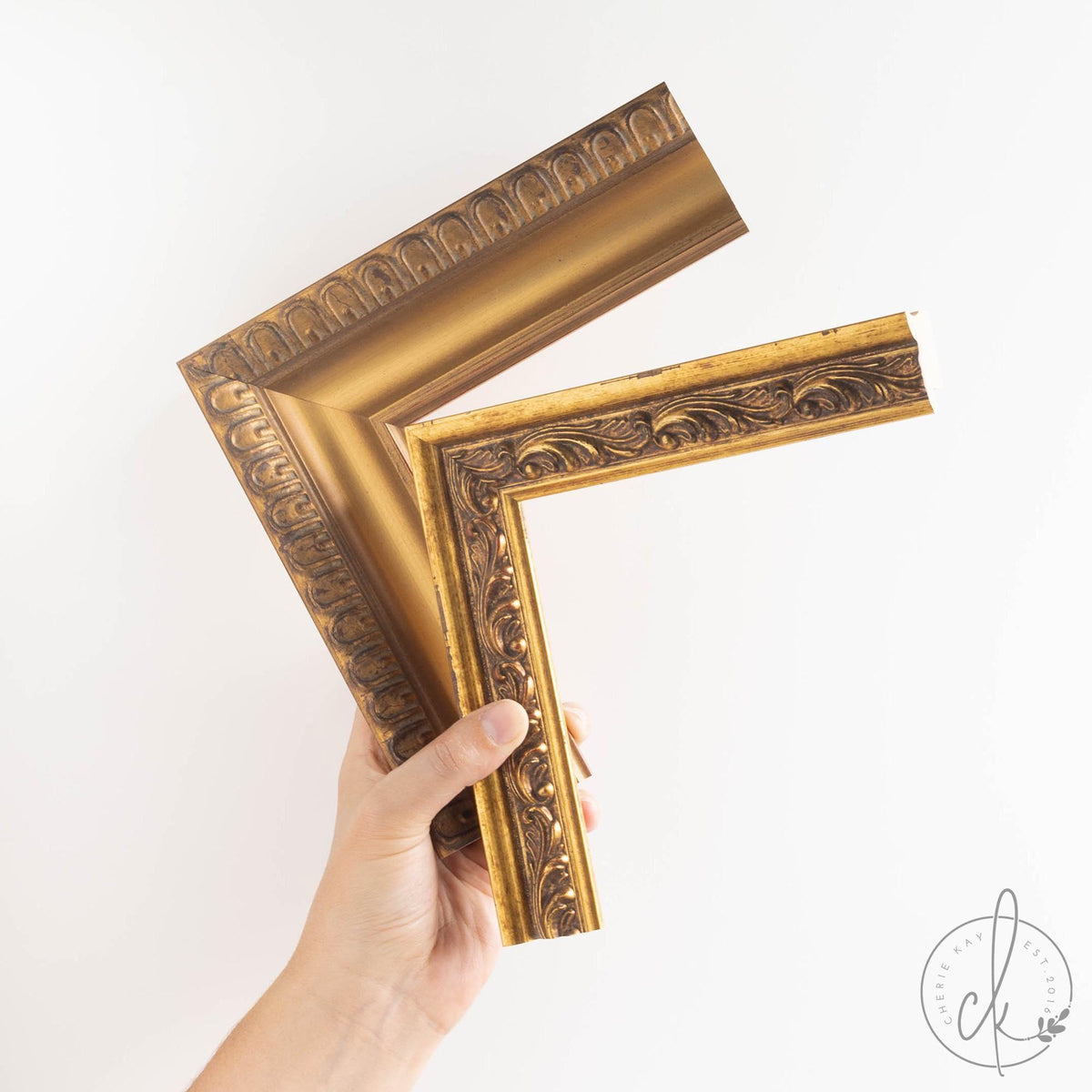 Hand holding two ornate gold wood frame corner samples side by side, showing different carved detail options for the antique horse print.