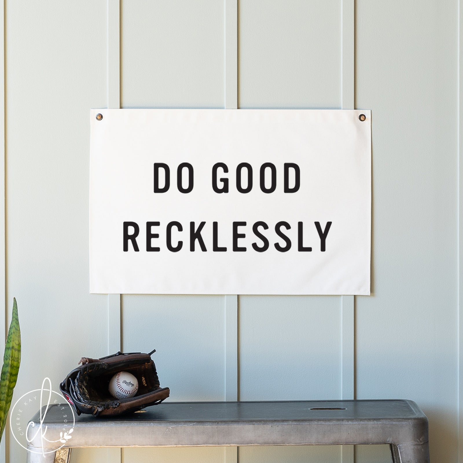Motivational sign with 'Do Good Recklessly' text on a white background, placed on a shelf with a baseball and glove.