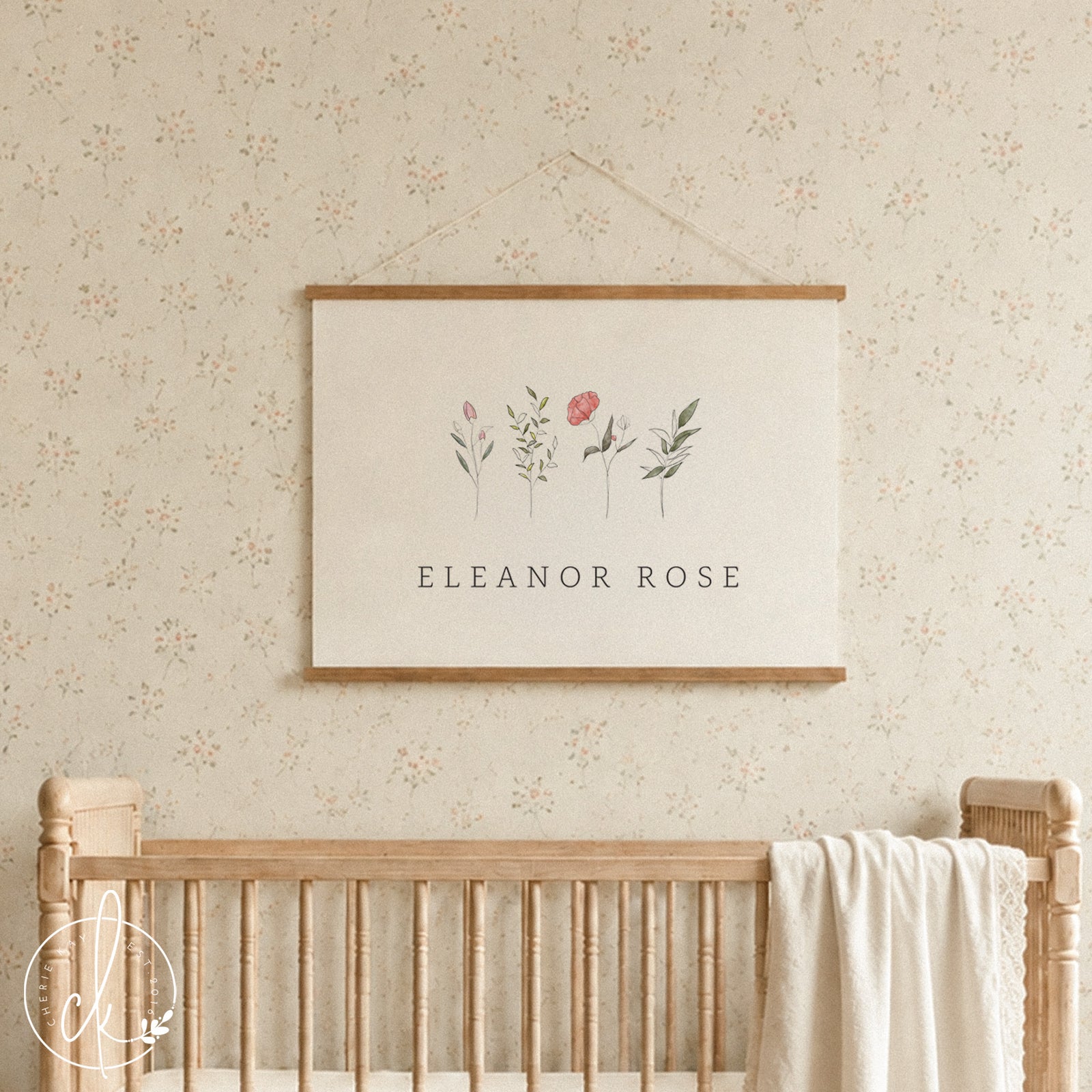 A white crib with a tan blanket and two pillows. A framed print with a floral design and the names "Evelyn Jo" hangs above the crib.