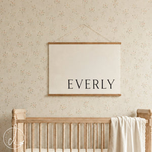 Custom nursery decor canvas banner with personalized baby name in serif lettering on cream canvas with wood strips