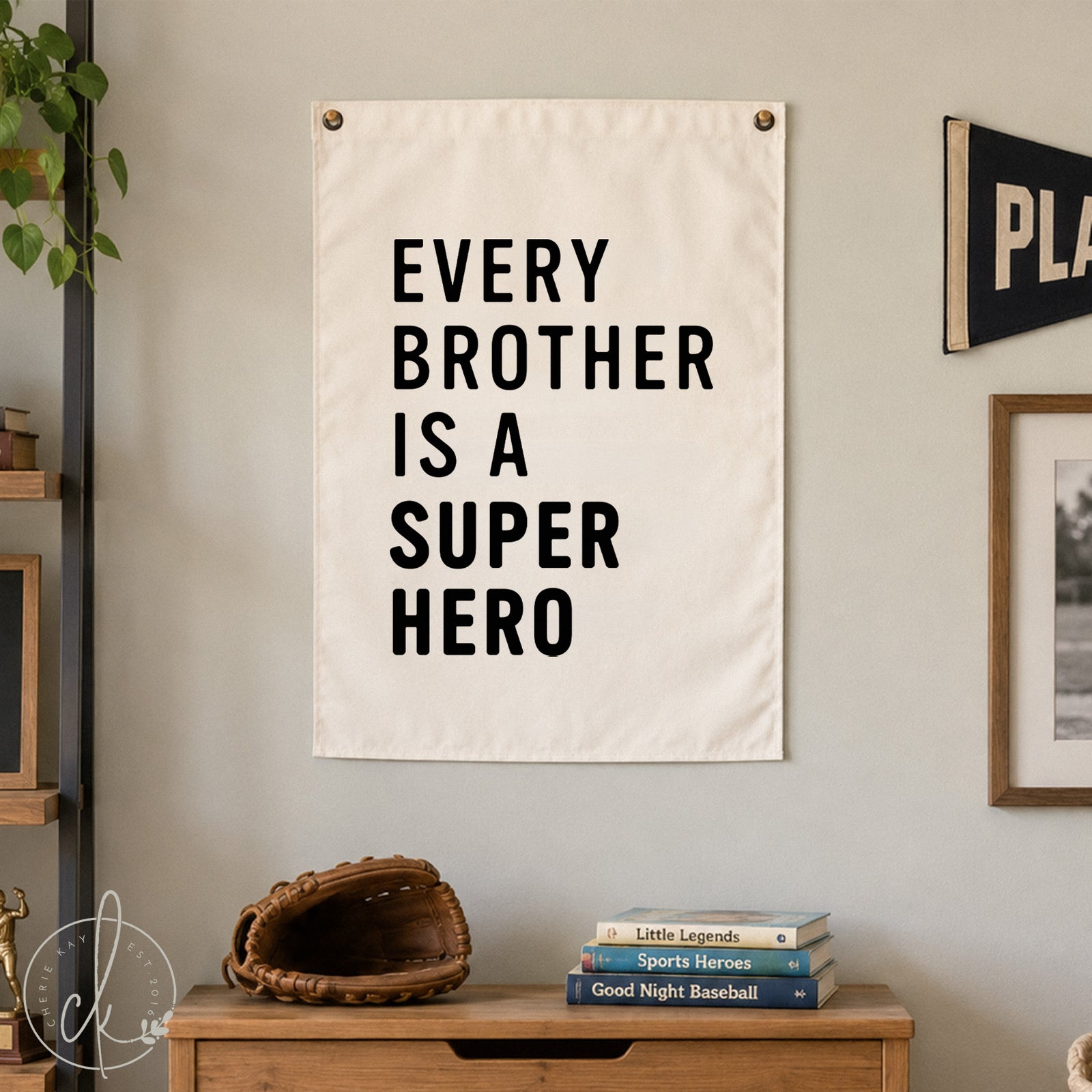 Canvas sign with the text "Every Brother is a Superhero" hanging on a white wall. Below the sign is a wooden chest with a baseball glove and books on top