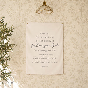 A white canvas wall tapestry with black text that reads "Fear not for I am with you be not dismayed for I am your God I will strengthen you I will help you I will uphold you with my righteous right hand. Isaiah 41:10". 