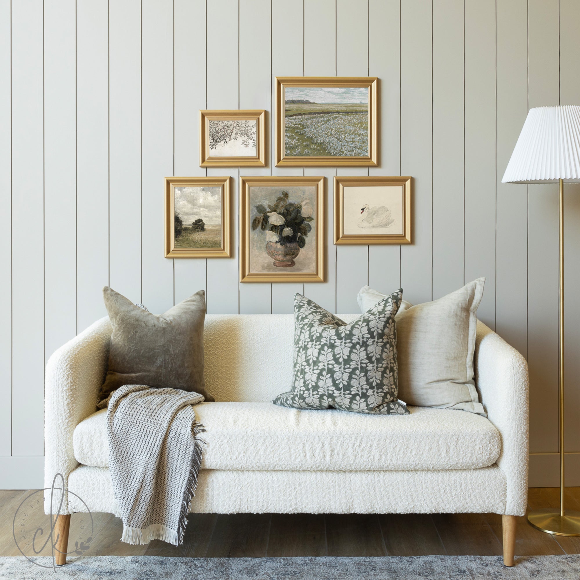 Cozy living room with a rustic gallery wall featuring five gold-framed art prints, including vintage landscapes, botanicals, and classic artwork, above a neutral sofa with accent pillows and a throw blanket.