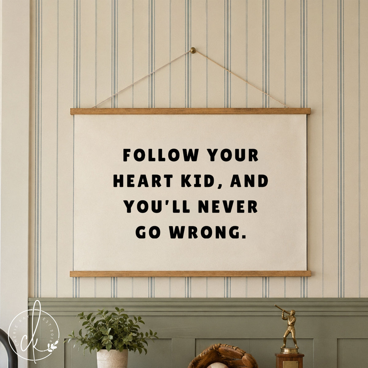 A white rectangular wall banner featuring the black text FOLLOW YOUR HEART KID, AND YOU'LL NEVER GO WRONG. The banner is mounted wood strips and string, and hangs over a boys dresser