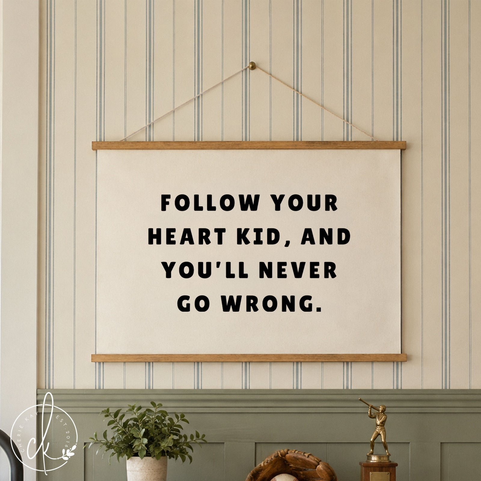 A white rectangular wall banner featuring the black text FOLLOW YOUR HEART KID, AND YOU'LL NEVER GO WRONG. The banner is mounted wood strips and string, and hangs over a boys dresser