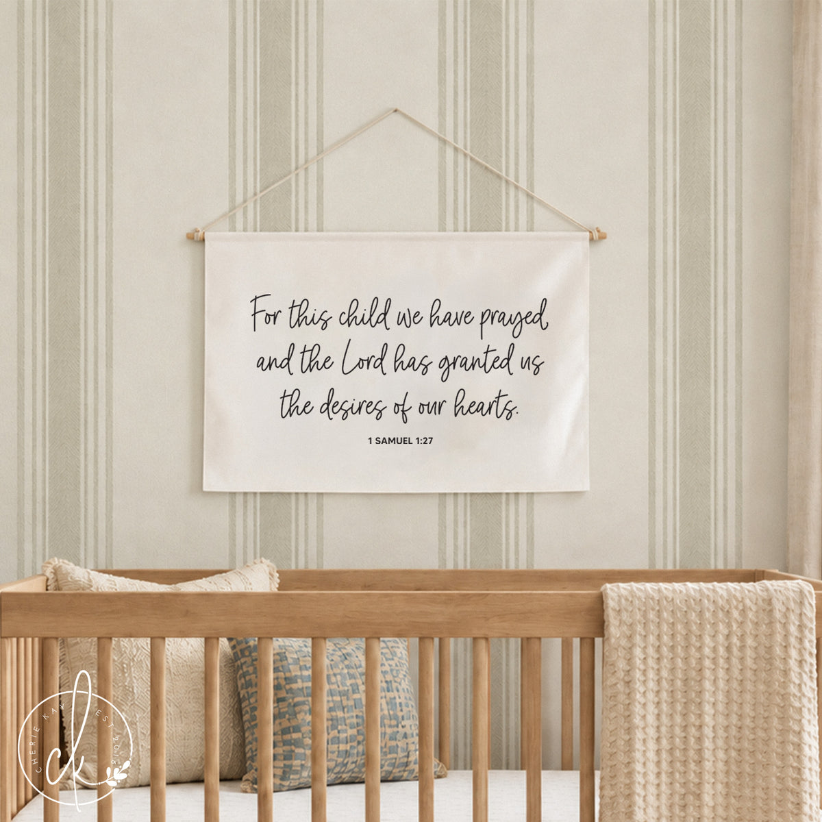 A rectangular off-white fabric wall hanging featuring the black printed text: For this child we have prayed and the Lord has granted us the desires of our hearts 1 SAMUEL 1:27. The banner is suspended by a thin white string.