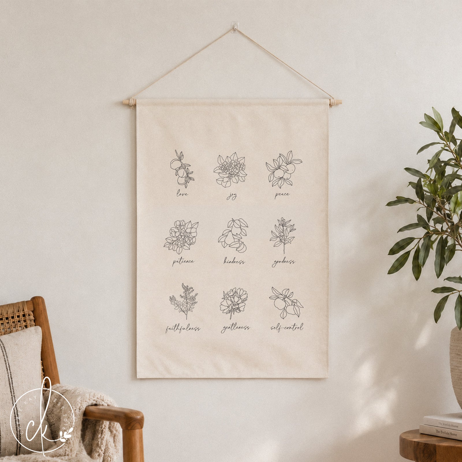 A white canvas wall hanging with black line drawings of flowers and the words "love", "joy", "peace", "patience", "kindness", "goodness", "faithfulness", "gentleness", and "self-control".