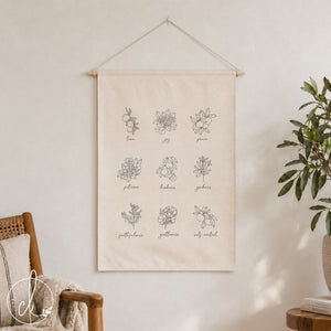 A white canvas wall hanging with black line drawings of flowers and the words "love", "joy", "peace", "patience", "kindness", "goodness", "faithfulness", "gentleness", and "self-control".