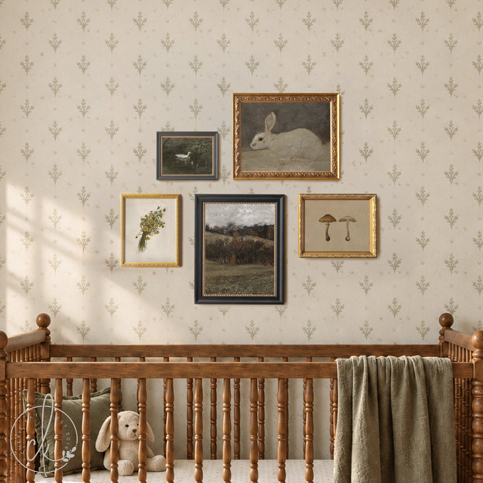 A wooden crib with a cream mattress and a textured green throw blanket. Above the crib, five framed art prints are displayed on the wall, featuring a rabbit, a landscape, mushrooms, and botanical illustrations